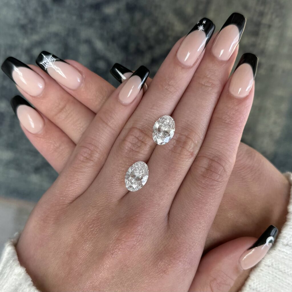 Pair of Fancy-shape (Oval) Diamonds, one with official "Excellent" Cut Grade and the other without, laid out on a young lady's hand